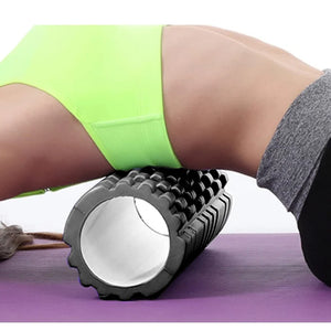 Person using a foam roller on a purple mat with green shorts and gray leggings.